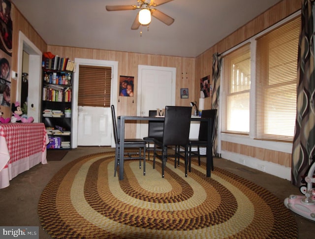 dining area featuring ceiling fan and wooden walls