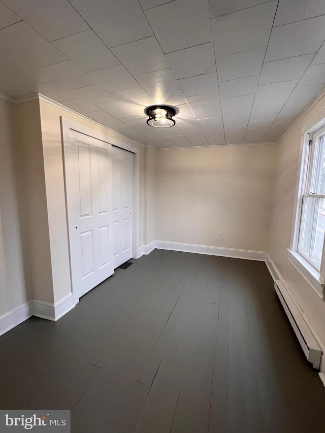 empty room with dark hardwood / wood-style floors, baseboard heating, and crown molding