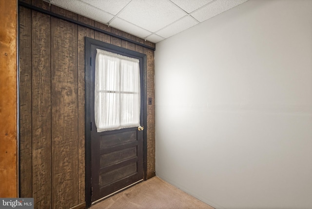 entryway with carpet, a paneled ceiling, and wooden walls