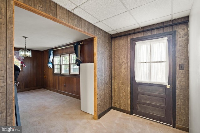 entryway with a paneled ceiling, light colored carpet, wooden walls, and an inviting chandelier