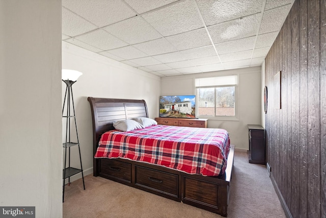 bedroom featuring a drop ceiling, light colored carpet, and wooden walls