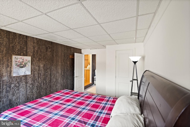 bedroom featuring a paneled ceiling and wood walls