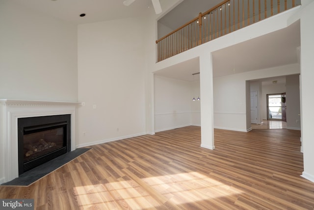 unfurnished living room featuring ceiling fan, a high ceiling, and hardwood / wood-style flooring