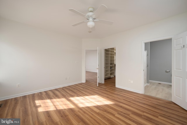 unfurnished bedroom with a walk in closet, ceiling fan, a closet, and hardwood / wood-style flooring