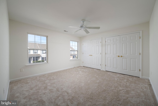 unfurnished bedroom with ceiling fan, light colored carpet, and two closets