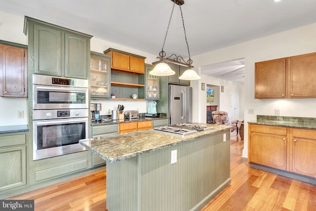 kitchen featuring pendant lighting, stone counters, light hardwood / wood-style flooring, appliances with stainless steel finishes, and a kitchen island