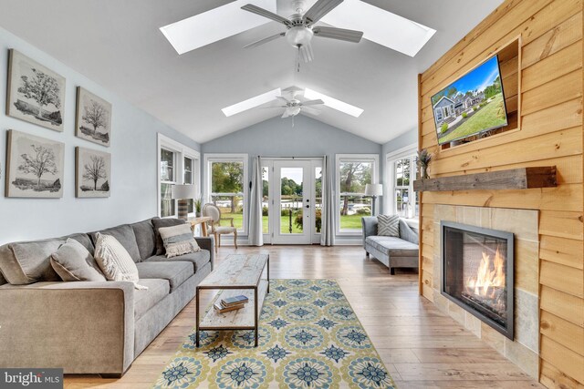 living room with ceiling fan, light wood-type flooring, a tile fireplace, and vaulted ceiling