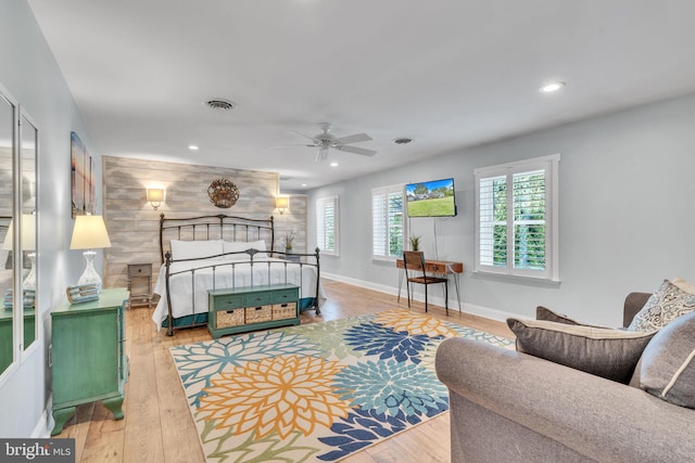 bedroom featuring ceiling fan, light hardwood / wood-style flooring, and wooden walls