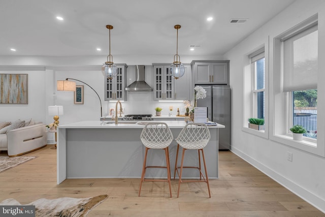 kitchen featuring appliances with stainless steel finishes, wall chimney exhaust hood, light hardwood / wood-style floors, decorative light fixtures, and gray cabinets