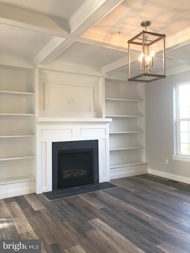 unfurnished living room with built in shelves, ornamental molding, dark wood-type flooring, and an inviting chandelier