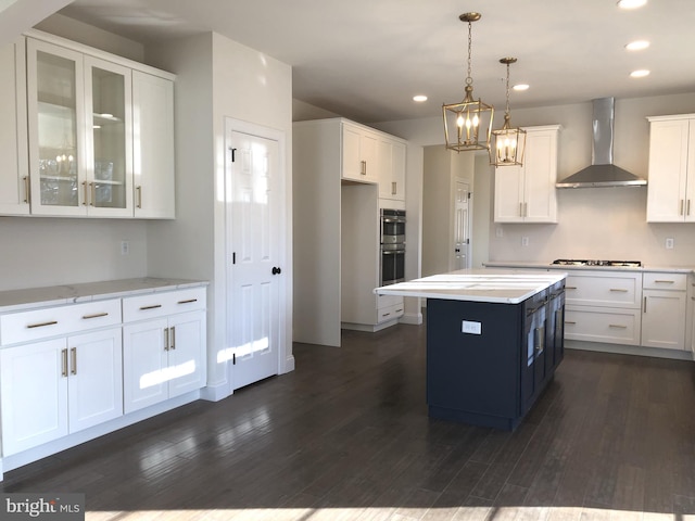 kitchen featuring a center island, dark wood-type flooring, wall chimney range hood, decorative light fixtures, and white cabinetry