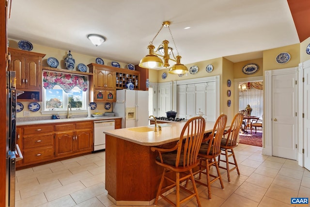 kitchen featuring sink, an island with sink, decorative light fixtures, white appliances, and a breakfast bar