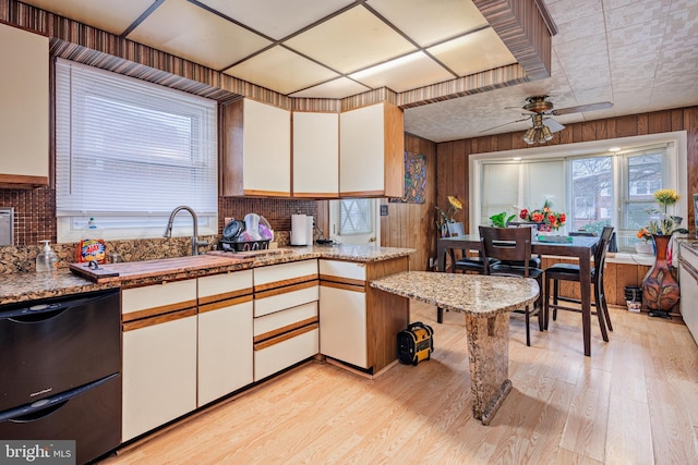 kitchen with white cabinetry, dishwasher, ceiling fan, wood walls, and light hardwood / wood-style floors