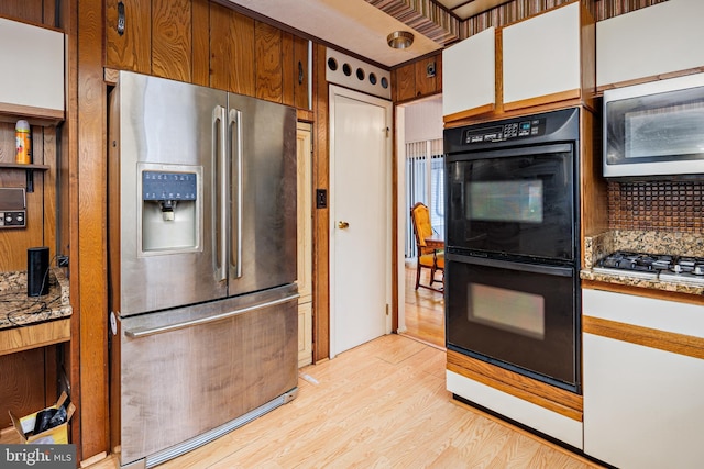 kitchen with decorative backsplash, stainless steel appliances, white cabinetry, and light hardwood / wood-style floors