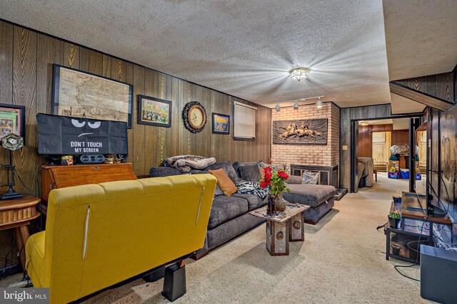 carpeted living room with a textured ceiling, wood walls, track lighting, and a brick fireplace