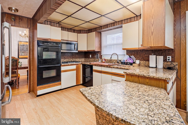 kitchen featuring kitchen peninsula, light stone counters, black appliances, and light wood-type flooring