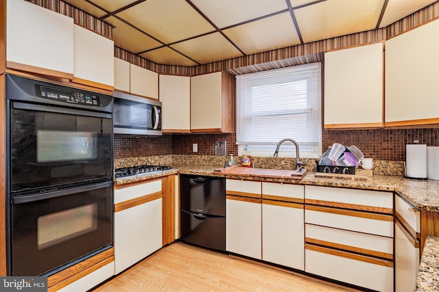 kitchen with white cabinetry, sink, light stone counters, light hardwood / wood-style floors, and black appliances