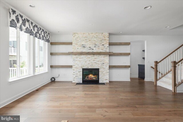 unfurnished living room featuring hardwood / wood-style flooring and a stone fireplace