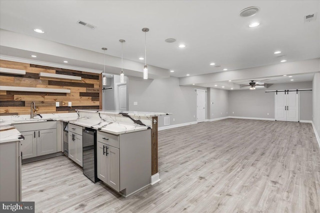 kitchen with light stone countertops, light wood-type flooring, a barn door, decorative light fixtures, and gray cabinets