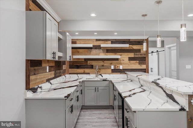 kitchen featuring kitchen peninsula, a barn door, decorative light fixtures, and light stone counters