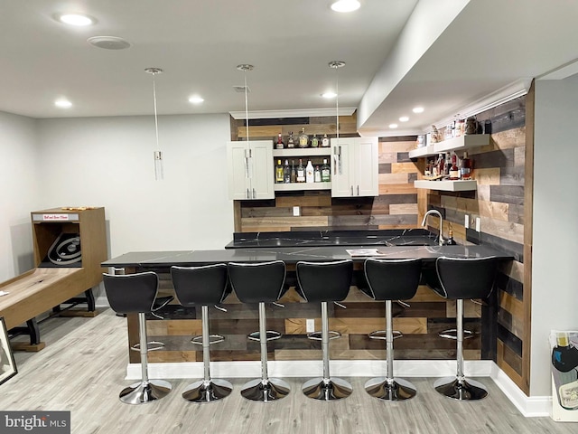 bar with backsplash, white cabinets, decorative light fixtures, and light wood-type flooring