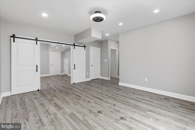 unfurnished bedroom featuring a barn door and light hardwood / wood-style floors