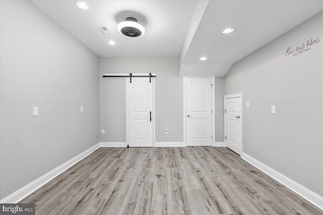 unfurnished bedroom with light wood-type flooring and a barn door