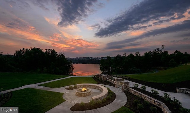 patio terrace at dusk with a yard, a water view, and an outdoor fire pit