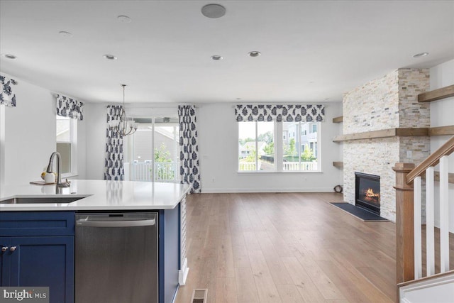 kitchen with a fireplace, blue cabinets, sink, light hardwood / wood-style flooring, and dishwasher