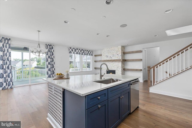 kitchen featuring hardwood / wood-style floors, sink, stainless steel dishwasher, an island with sink, and a notable chandelier