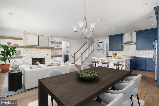 dining area with a stone fireplace, wood-type flooring, and an inviting chandelier