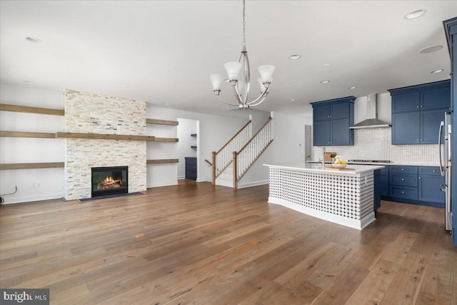 kitchen featuring blue cabinetry, wall chimney exhaust hood, dark hardwood / wood-style floors, a chandelier, and a center island with sink