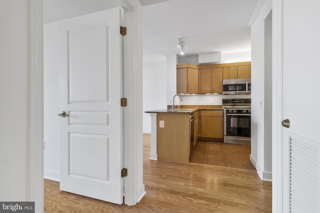 kitchen with light hardwood / wood-style floors, kitchen peninsula, sink, and appliances with stainless steel finishes