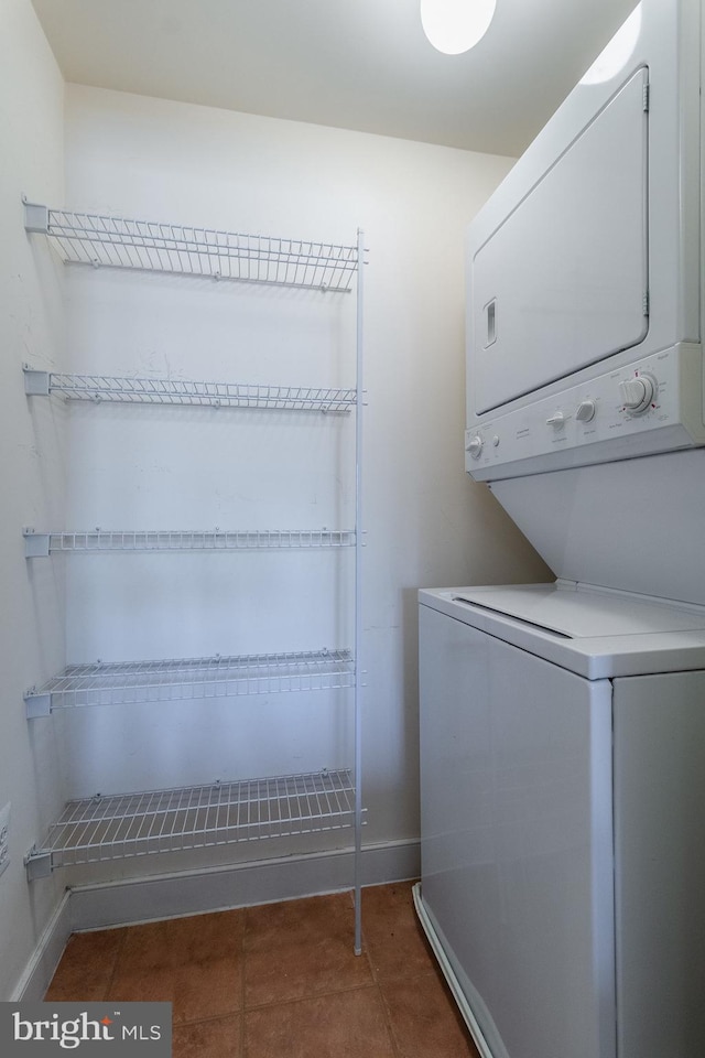 laundry room with dark tile patterned floors and stacked washer and dryer