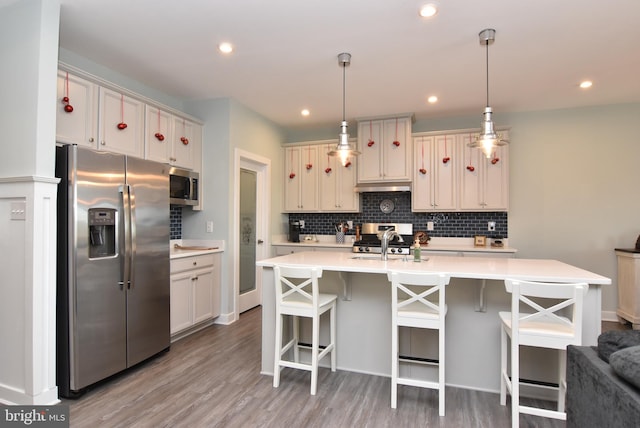 kitchen featuring a kitchen bar, stainless steel appliances, decorative light fixtures, hardwood / wood-style floors, and an island with sink