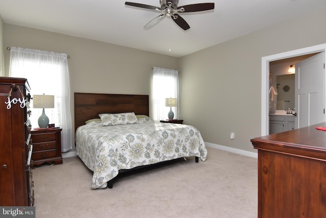 bedroom with connected bathroom, ceiling fan, light colored carpet, and multiple windows