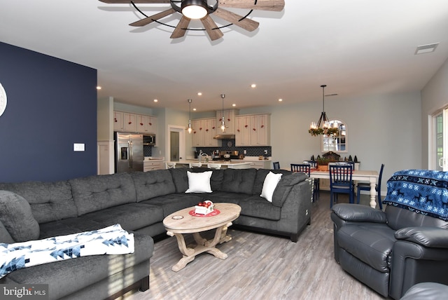 living room featuring ceiling fan with notable chandelier and light hardwood / wood-style flooring