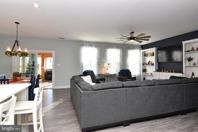 living room with ceiling fan with notable chandelier and wood-type flooring