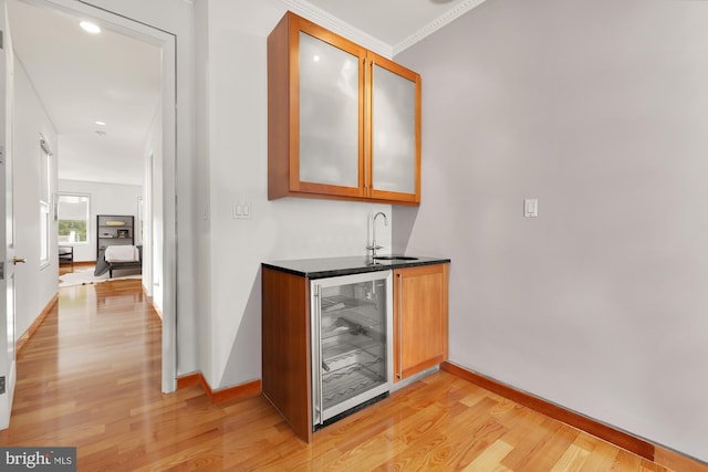 bar with light hardwood / wood-style flooring, beverage cooler, ornamental molding, and sink