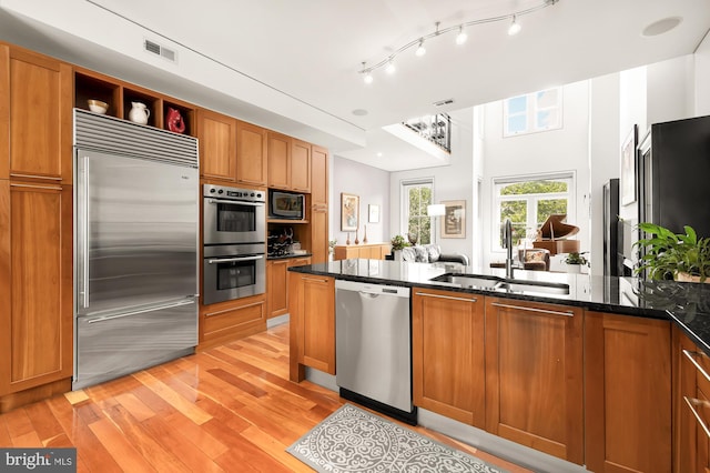 kitchen with sink, light hardwood / wood-style flooring, kitchen peninsula, built in appliances, and dark stone counters