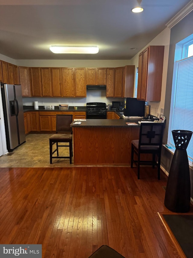 kitchen featuring a kitchen breakfast bar, kitchen peninsula, black appliances, and dark hardwood / wood-style floors