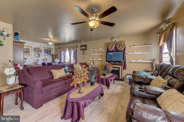 living room featuring light wood-style flooring, ceiling fan, and a glass covered fireplace