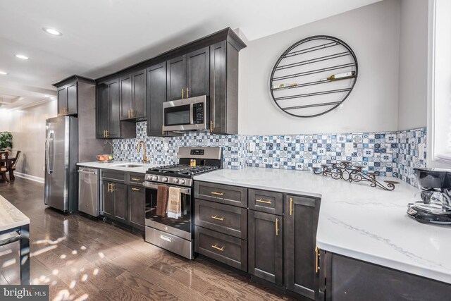 kitchen featuring sink, light stone counters, dark hardwood / wood-style floors, decorative backsplash, and appliances with stainless steel finishes