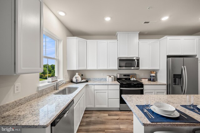 kitchen with white cabinets, sink, light stone countertops, light wood-type flooring, and appliances with stainless steel finishes