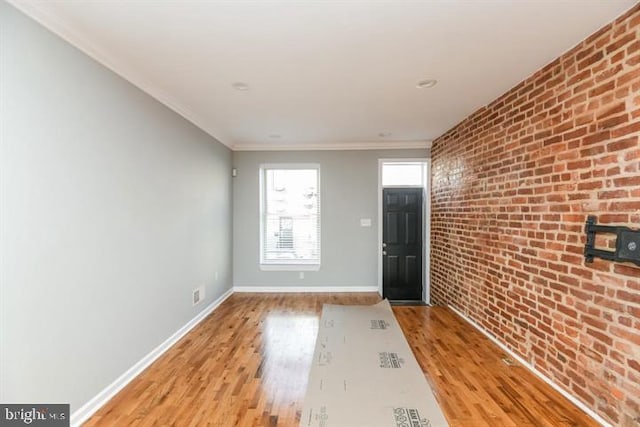 entryway with light hardwood / wood-style floors, brick wall, and ornamental molding