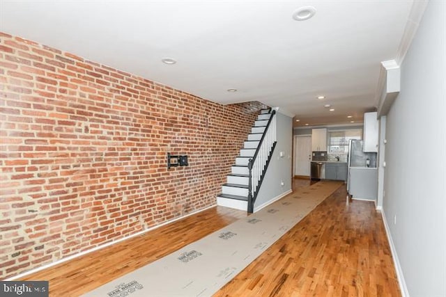 hall with crown molding, brick wall, and light wood-type flooring