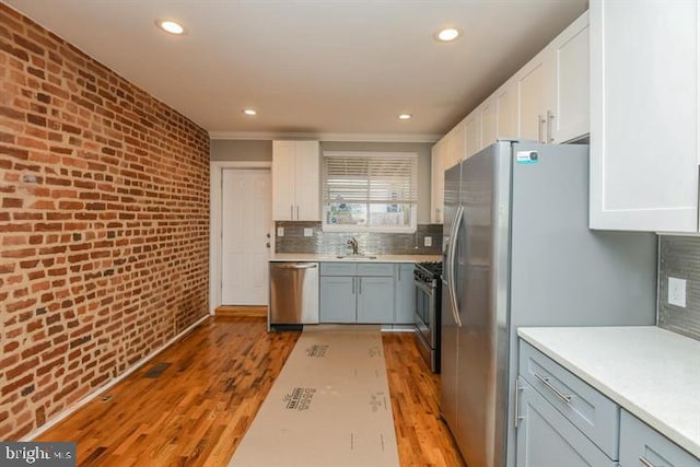 kitchen with white cabinets, light hardwood / wood-style floors, stainless steel appliances, and brick wall