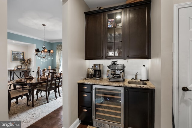 bar with sink, backsplash, beverage cooler, dark brown cabinets, and light stone countertops