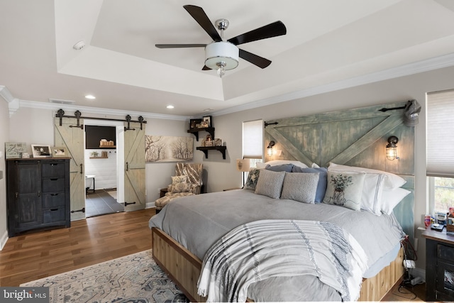 bedroom featuring ornamental molding, a raised ceiling, wood-type flooring, and a barn door