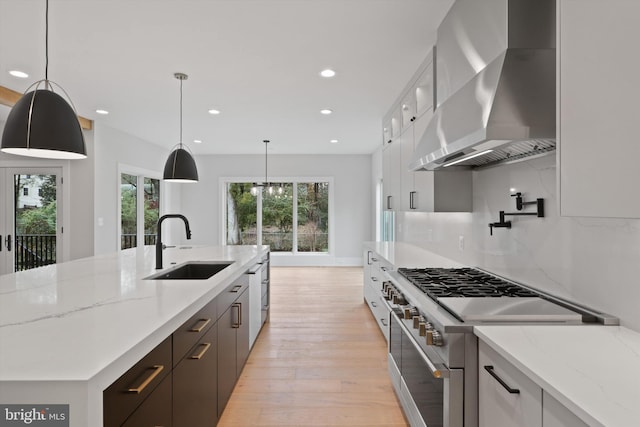 kitchen with white cabinetry, sink, wall chimney exhaust hood, light hardwood / wood-style floors, and appliances with stainless steel finishes